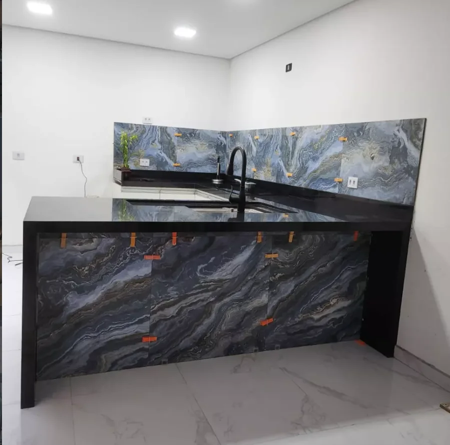 Bancada preta com frontão e frente em pedra azul de veios ondulados, obra da Completa